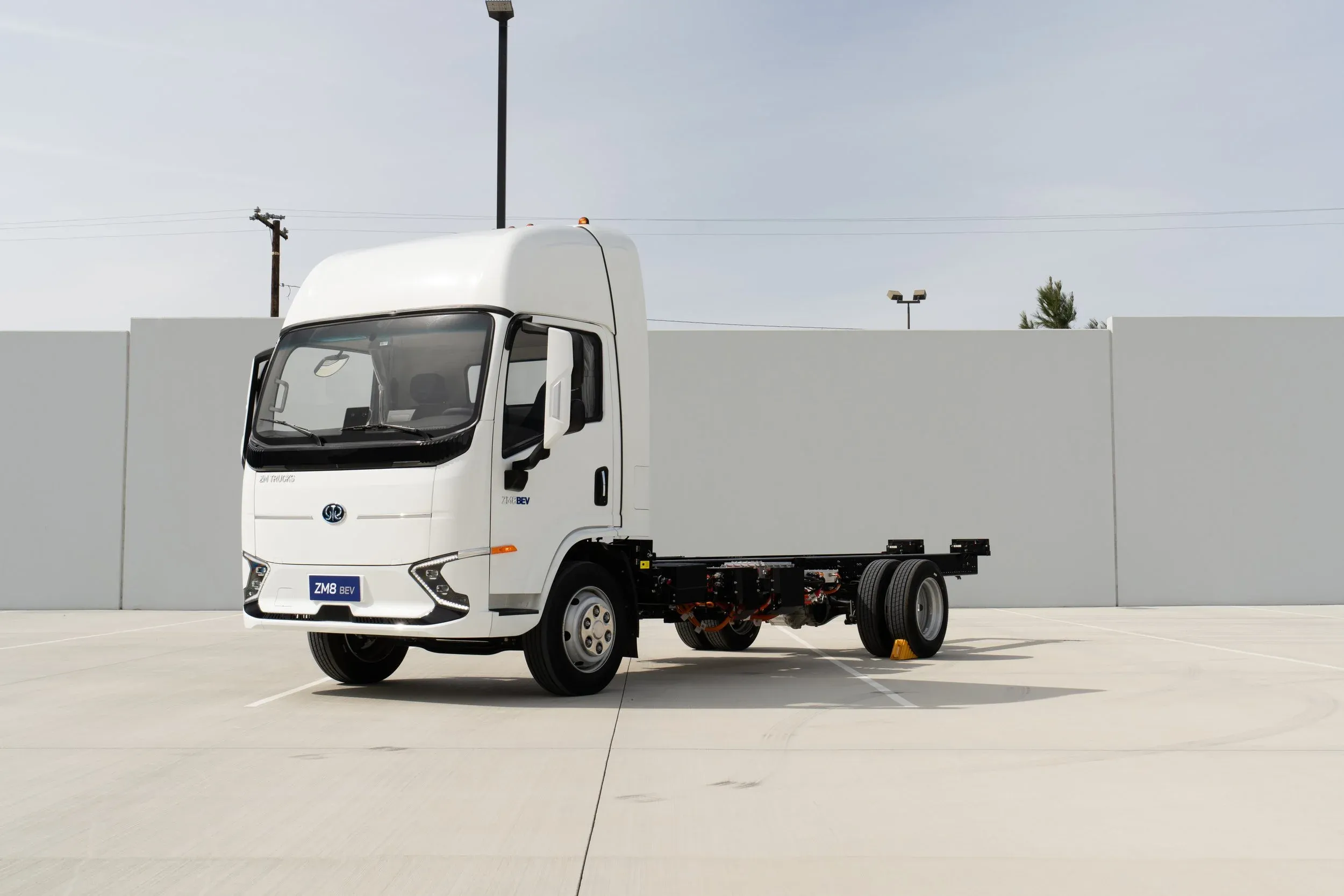 White electric truck with no cargo bed in front of a gray wall